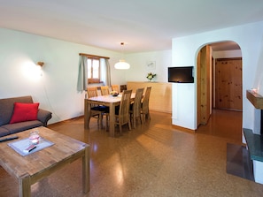 A compact living space with a dining area, a sofa, a coffee table, a TV, and a wooden door. - Ferienhaus Muntschi, (Andeer), by Interhome (Andeer)