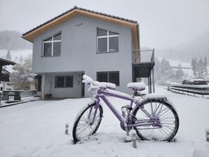 Un immeuble de deux étages avec un balcon, un vélo appuyé contre le mur et de la neige au sol.
