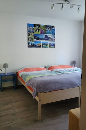 Ein Schlafzimmer mit einem hölzernen Bett, einem Nachttisch mit Lampe und einem Wandbild von Landschaften.