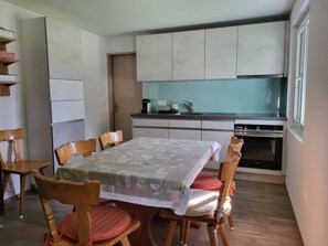 A compact kitchen with a dining table, chairs, and a refrigerator. - Engadinella, (Splügen), by Interhome (Splügen)