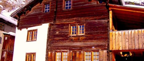A rustic wooden building with multiple windows, a balcony, and a snow-covered landscape in the background.