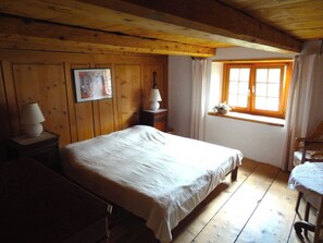 Ein Schlafzimmer mit Holzwandverkleidung, einem Bett, einem Nachttisch, einer Lampe und einem Fenster mit Vorhängen.