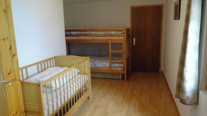 A room with a wooden crib, a bunk bed, and a door.