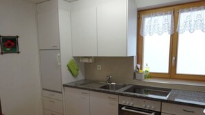 A kitchen with white cabinets, a double sink, a stove, and a window with lace curtains.