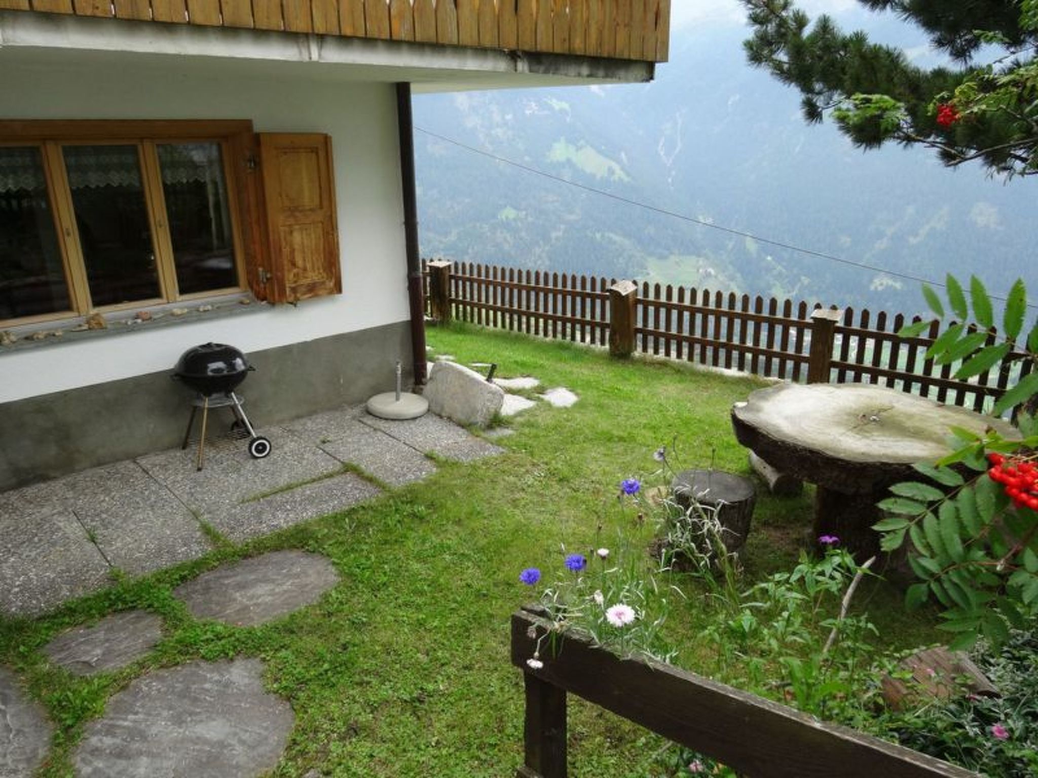 Een huis met een stenen pad dat leidt naar een houten terras, een barbecue en een stenen waterput.