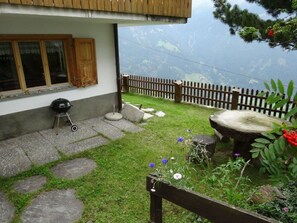 A house with a stone pathway leading to a wooden deck, a barbecue grill, and a stone well. - Tgea Beala Vesta, (Lohn), by Interhome (Lohn GR)