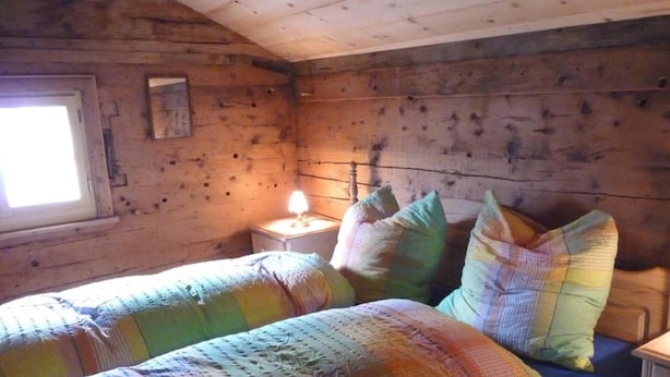 Una habitación tipo cabaña con dos camas, una mesita de noche, una lámpara y una ventana.