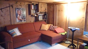 Una habitación acogedora con techo de madera, un sofá rojo, una estantería y un cuadro en la pared.