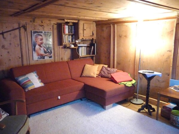 A cozy room with a wooden ceiling, a red sofa, a bookshelf, and a framed picture on the wall.