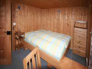 A wooden-paneled room with a bed, a dresser, and a chair.
