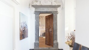 A hallway with a classical archway, a wooden door, and a framed artwork on the wall.