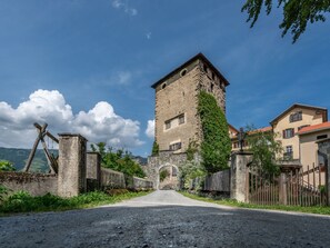 Ein historischer SteinTurm mit schmalem Eingang, umgeben von einem rustikalen Zaun und einer gepflasterten Straße, die darauf führt.