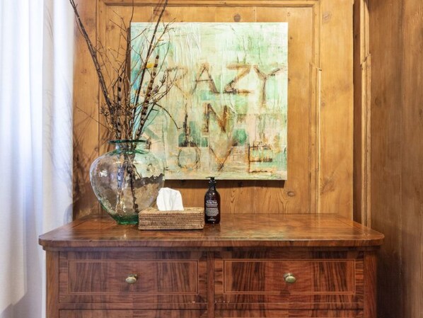 Un mueble de madera con un florero de vidrio que contiene ramas, una caja de pañuelos y una botella de gel antibacterial.