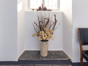 Une pièce avec un mur blanc, une fenêtre décorée de pommes de pin et une chaise en bois.