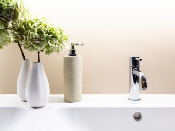 A bathroom sink with a modern faucet, two white vases with green plants, and a cylindrical soap dispenser.
