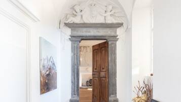 A hallway with a classical architectural archway, wooden doors, and a framed artwork on the wall.