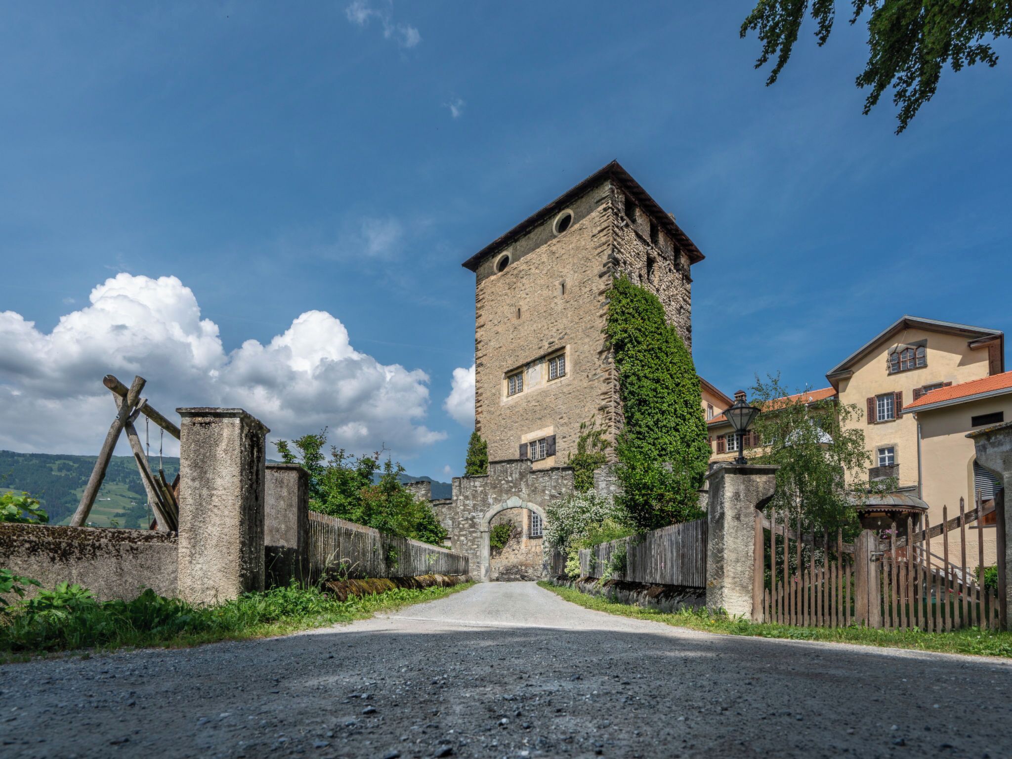 A historic stone tower with a narrow entrance, surrounded by traditional buildings and a gravel road.