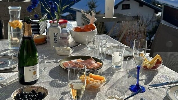 Mesa posta com comida e bebidas, uma garrafa de champanhe e uma vista panorâmica das montanhas.
