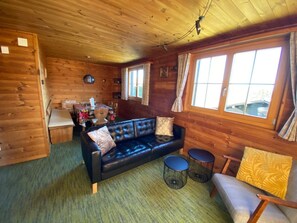 A cozy cabin interior with a wooden interior, a black leather sofa, a dining table, and two round tables.