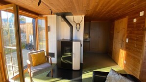 Um interior em madeira com lareira, um sofá, uma área de refeições e uma porta de vidro deslizante que dá para um espaço ao ar livre.