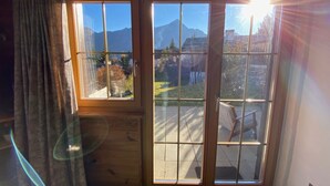 Quarto com piso de madeira, janela com vista para montanhas e cortina.