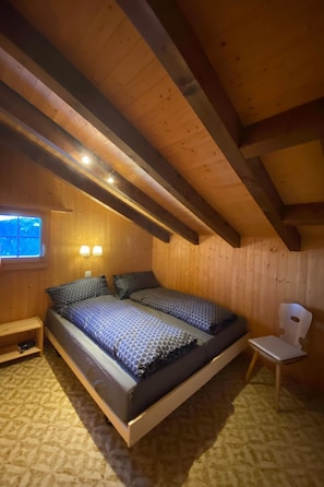 A wooden cabin bedroom with a bed, two wall-mounted lights, a window, and a chair. - Haus Maran, (Oberurmein), by Interhome (Urmein)
