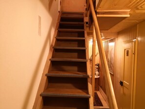 A wooden staircase with a handrail, leading to a room with a door and a small window.