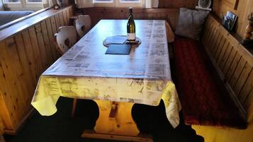 Ein Holztisch mit einer mit Zeitung bedeckten Oberfläche, eine Weinflasche und eine Bank mit Kissen.