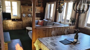 A cozy cabin-style room with a wooden bench, a table with a newspaper-covered tablecloth, and a television on a stand.