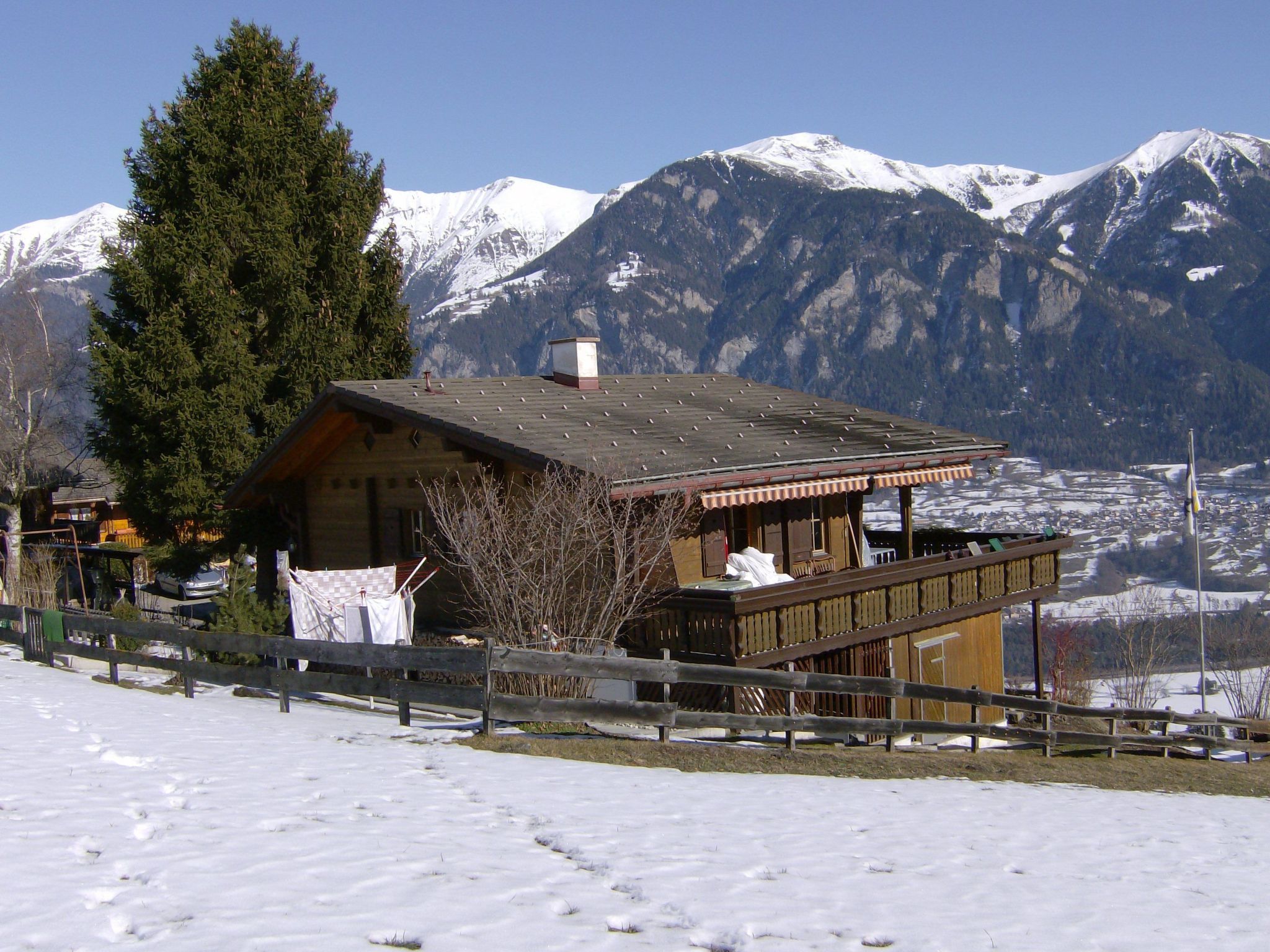 Un chalet doté d’un balcon en bois donnant sur un paysage enneigé et des montagnes.