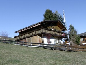Eine traditionelle Holzhütte mit Balkon, umgeben von einem Holzzaun und blauem Himmel.