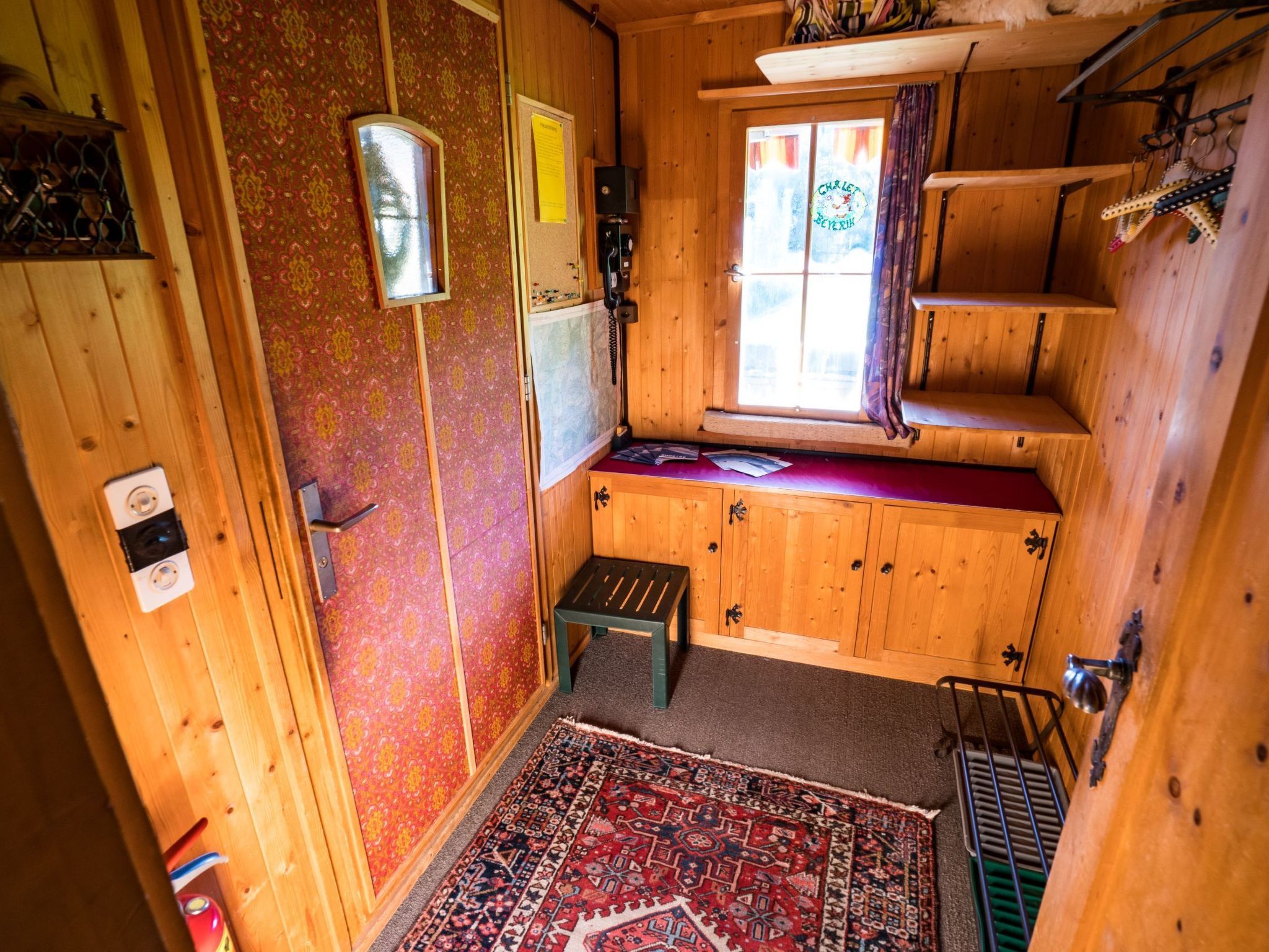 Ein Holzblockhaus-Interieur mit Fenster, kleinem Tisch und einem gemusterten Teppich.