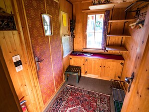Ein Holzblockhaus-Interieur mit Fenster, kleinem Tisch und einem gemusterten Teppich.