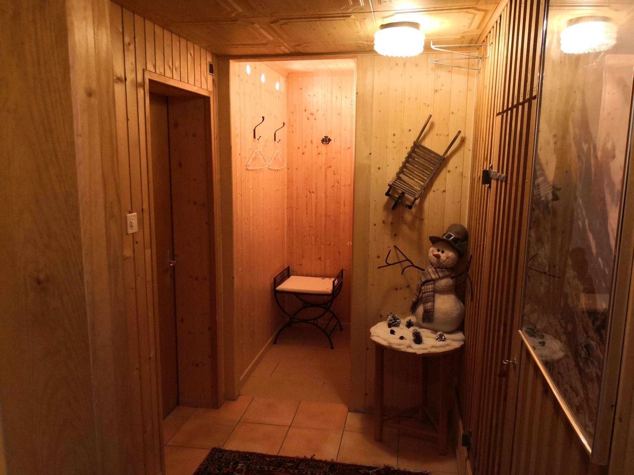 Un intérieur en bois avec un banc, un porte-objets fixé au mur et une décoration représentant un bonhomme de neige.