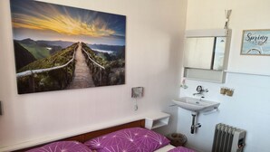 A bedroom with a bed, a painting of a landscape, a sink, and a radiator.