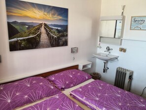 Een slaapkamer met een bed, een landschapsschilderij, een wastafel en een radiator.