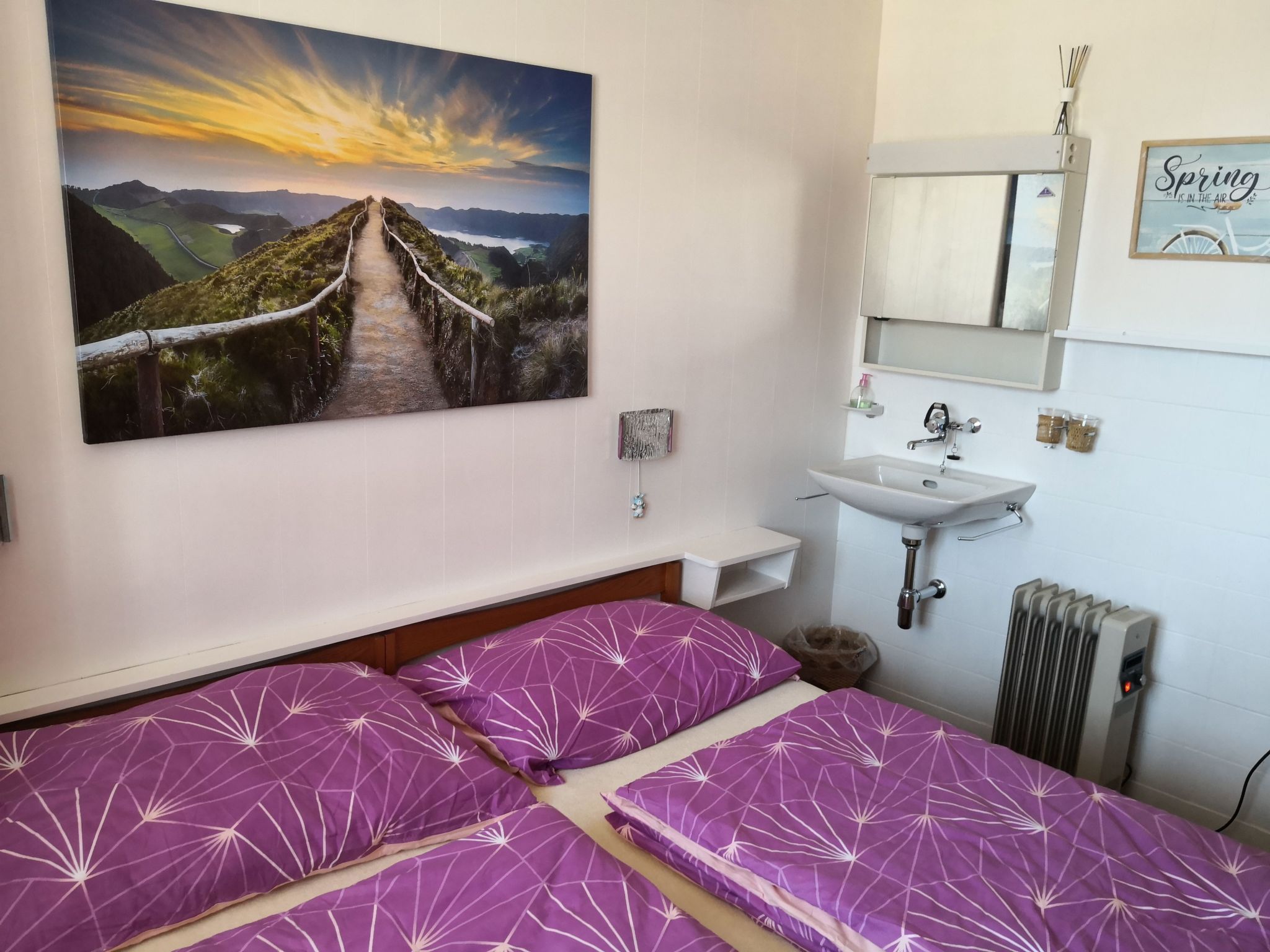 Une chambre avec deux lits, un tableau représentant un paysage, un lavabo et un radiateur.
