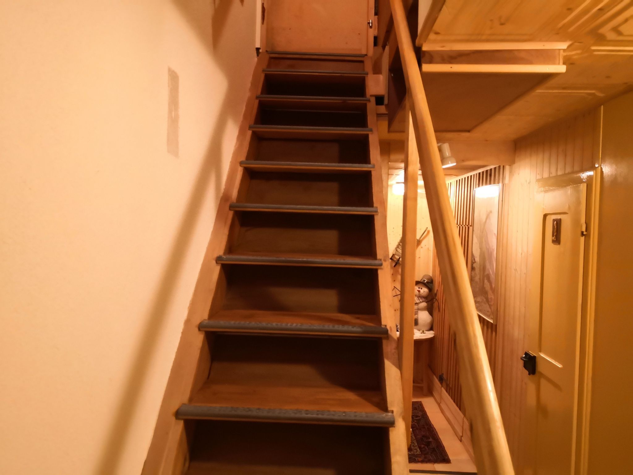 Una escalera de madera con barandilla que lleva a una puerta con un pequeño ventanal.