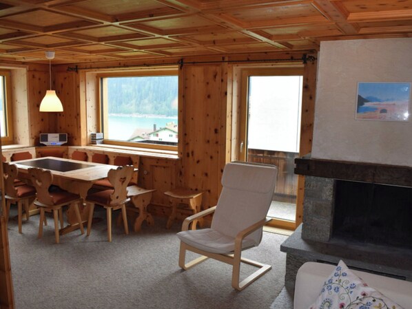A wooden cabin interior with a dining area, a fireplace, and large windows offering a view of a lake. - Wohnung Stücklihaus, (Sufers), by Interhome (Sufers)