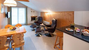 Un salon moderne comprenant un coin repas, une cuisine et un espace détente avec un téléviseur et une cheminée.
