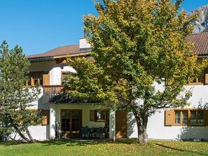 A two-story building with a white facade, a brown roof, and a large tree in front.
