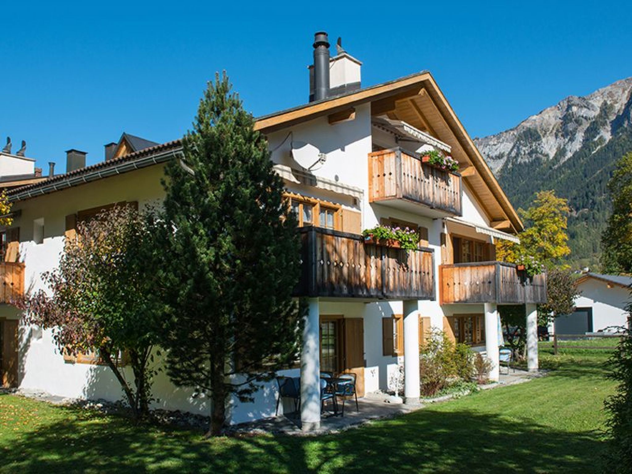 A two-story chalet with a balcony, a chimney, and a mountain backdrop.