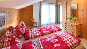 Une chambre avec deux lits, une commode en bois, une chaise et une fenêtre avec des rideaux.