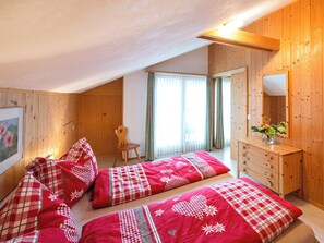 Ein Schlafzimmer mit zwei Betten, einer Holzkommode, einem Sessel und einem Fenster mit Vorhängen.