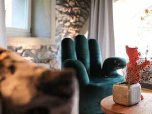 Une pièce comprenant un fauteuil turquoise, une table en bois avec un vase, et où l’on aperçoit une partie d’un canapé.