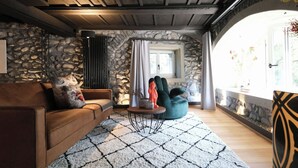 A cozy living room with a stone wall, a wooden ceiling, a brown sofa, a teal bean bag, and a patterned rug.