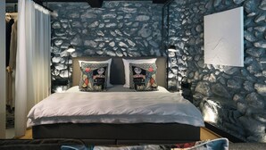 A bed with patterned pillows, a stone wall, and a mounted artwork.