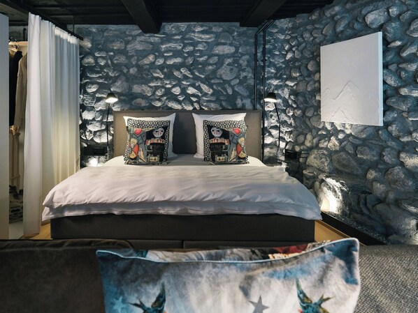 Una cama con almohadas estampadas, una pared de piedra y una obra de arte colgada.