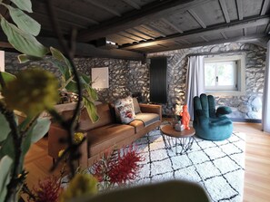 Una sala de estar acogedora con una pared de piedra, un sofá marrón, un sillón azul y una mesa de centro.