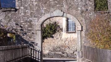 Un arco de piedra que conduce a un edificio con ventana, rodeado de un muro de piedra y una valla de madera.